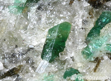 Photo of North Carolina emerald crystals from the Crabtree Emerald Mine. These crystals are embedded in a pegmatite that is rich in quartz, feldspar, black tourmaline, and bright green emerald. The emerald crystal in the center of the photo is only about 1/4 inch in length. Emerald-rich pieces of pegmatite from the Crabtree Mine are often slabbed and used to make interesting cabochons that display beautiful green emerald crystal cross-sections on a background of white pegmatite with a few crystals of black schorl tourmaline. 