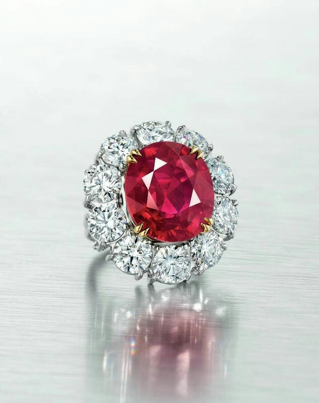 An exceptional 15.03 carat ‘pigeon blood’ Burmese ruby and diamond ring. Set with an oval-cut ruby, weighing approximately 15.03 carats, within a round brilliant-cut diamond surround, ring size 5 ¾, mounted in gold